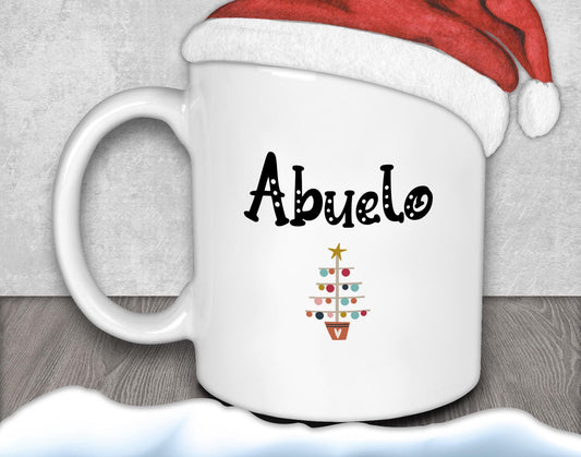 A white mug with the word &quot;Abuelo&quot; printed on it, along with a Christmas tree design, is placed on a wooden surface.