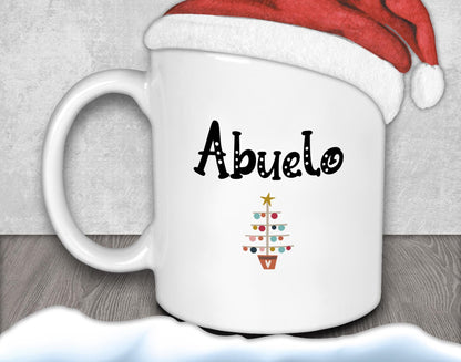 A white mug with the word &quot;Abuelo&quot; printed on it, along with a Christmas tree design, is placed on a wooden surface.