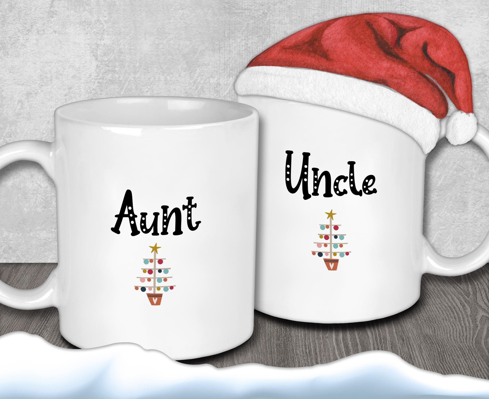 Two white mugs with the text &quot;Aunt&quot; and &quot;Uncle&quot; printed on them, along with a small Christmas tree design. A Santa hat is placed on top of one of the mugs.
