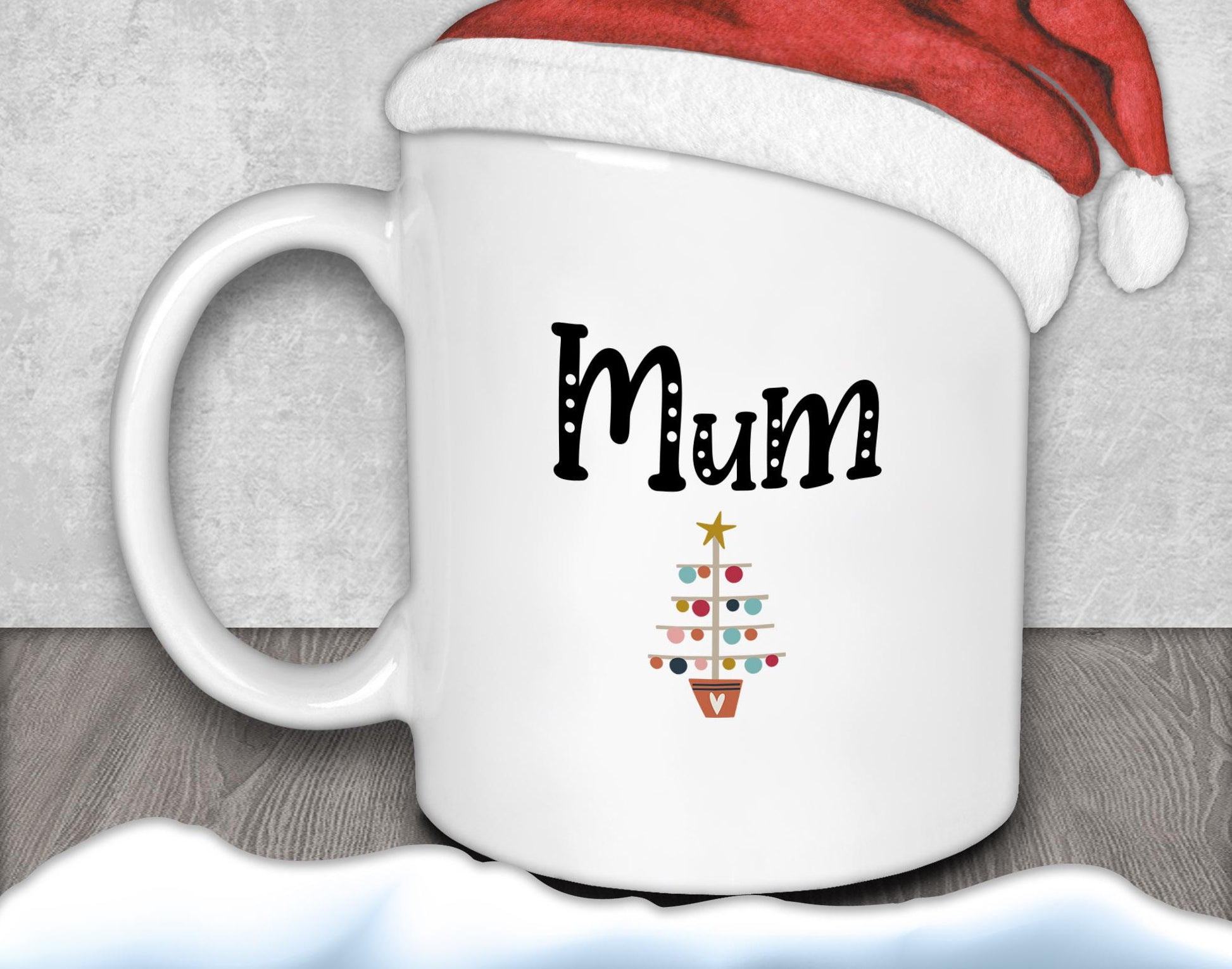 A white mug with the word &quot;Mum&quot; printed on it, along with a small Christmas tree design.