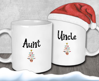 Two white mugs with the text &quot;Aunt&quot; and &quot;Uncle&quot; printed on them, along with a small Christmas tree design. A Santa hat is placed on top of one of the mugs.