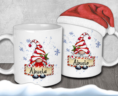 two white mugs with Christmas-themed designs, including gnomes and snowflakes. One mug has the name "Abuela" written on it, while the other mug has the name "Abuelo" written on it. Both mugs are decorated with festive elements, such as snowflakes and red and white striped gnomes.