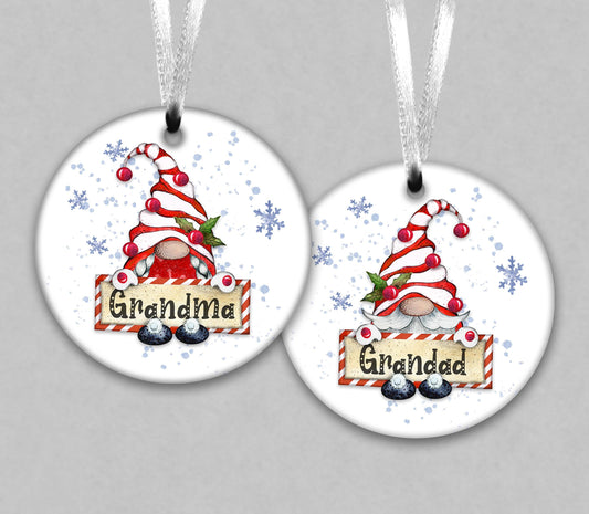 two round Christmas ornaments with a gnome theme. The gnomes are wearing red and white striped hats and are holding a sign that says &quot;Grandma&quot; and &quot;Grandad&quot;. The ornaments are hanging from strings, and there are snowflakes in the background.