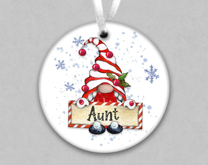 A white ornament with a gnome-like figure holding a sign that says &quot;Aunt&quot; and surrounded by snowflakes.