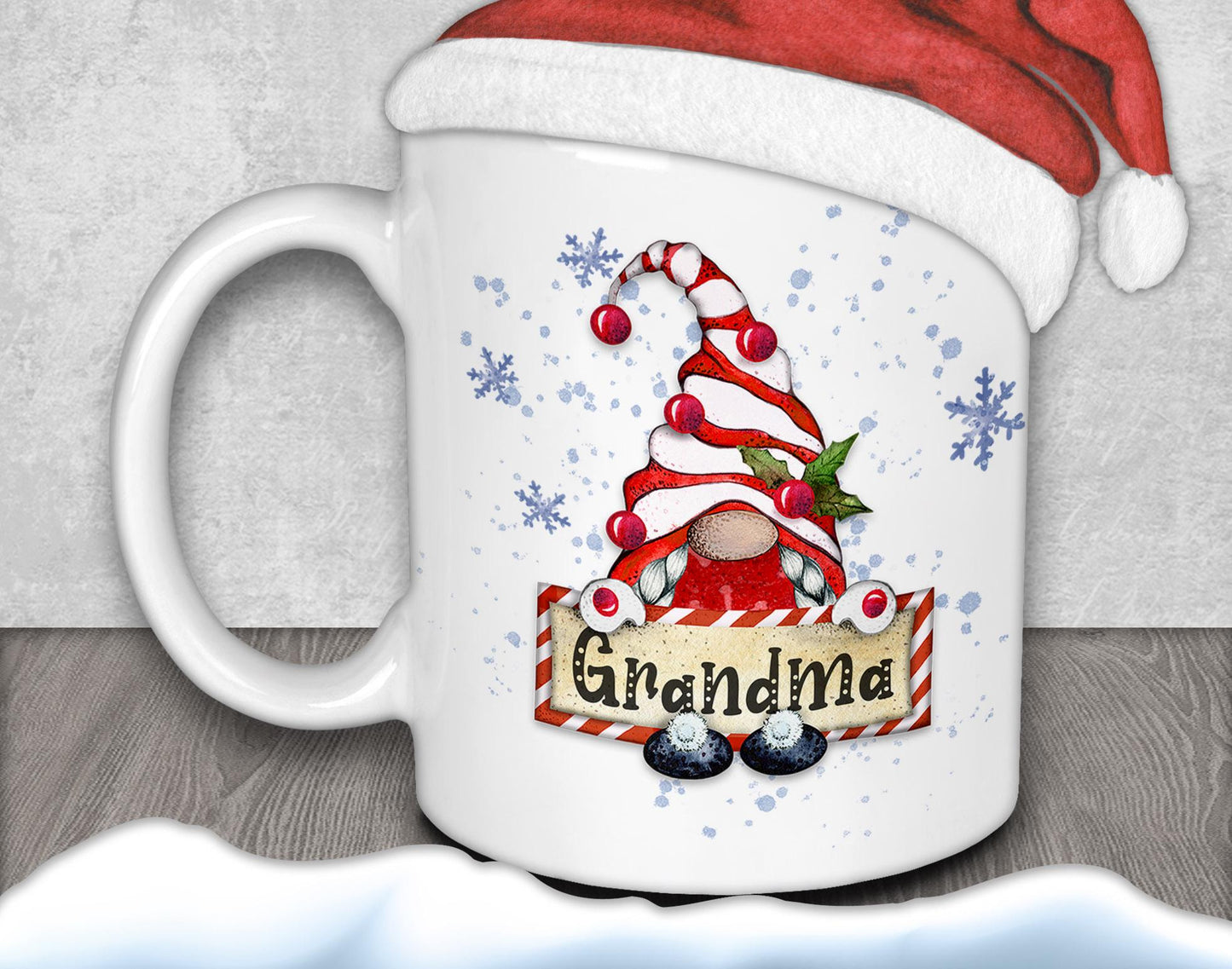 A white mug with a red and white striped gnome design and the word "Grandma" written on it, along with snowflakes and a Santa hat.