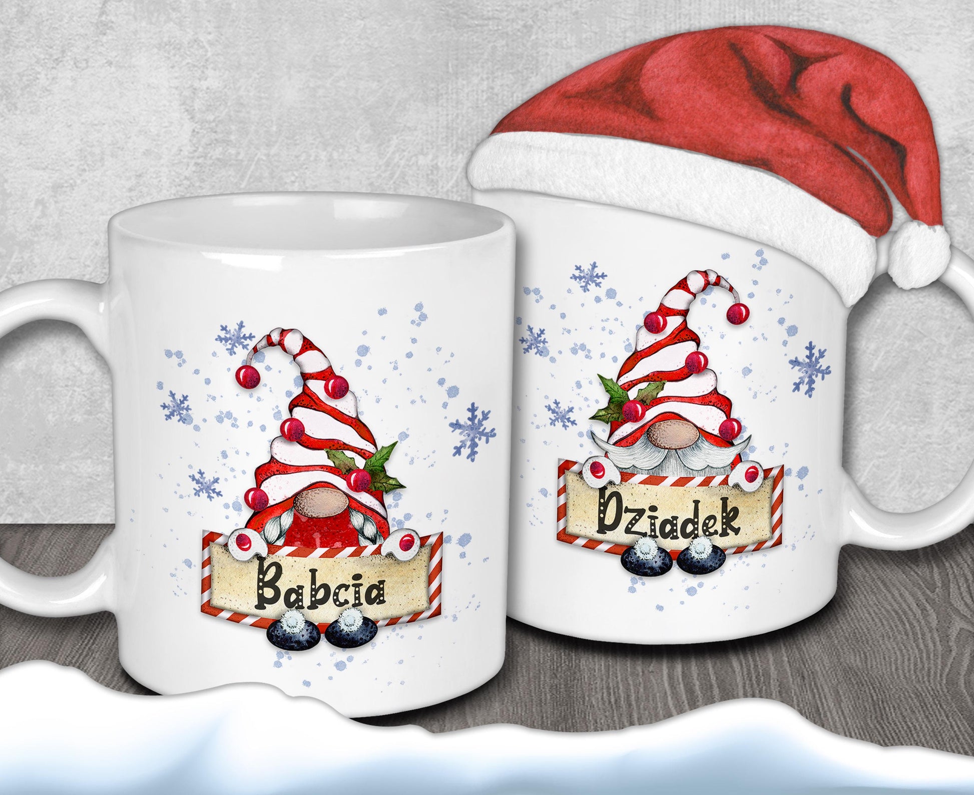 two white mugs with Christmas-themed designs, including gnomes and snowflakes. One mug has the name "Babcia" written on it, while the other mug has the name "Działek". A Santa hat is also present in the image.