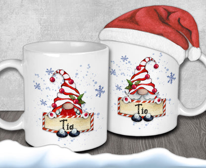 two white mugs with Christmas-themed designs, including gnomes and snowflakes. One mug has a Santa hat on top, and the other mug has the name "Tio" written on it.