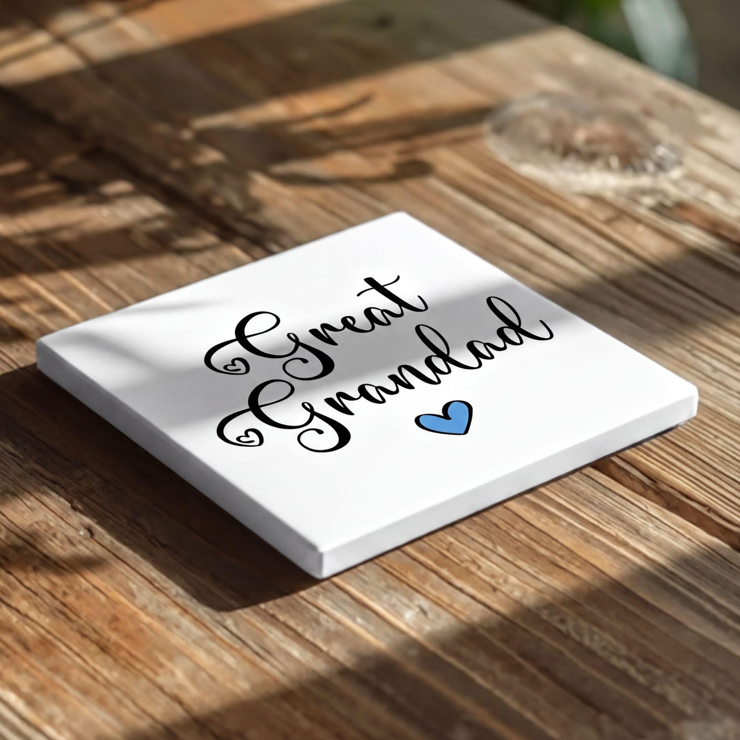 A white square coaster with the text "Great Grandad" and a blue heart symbol on it, placed on a wooden surface.
