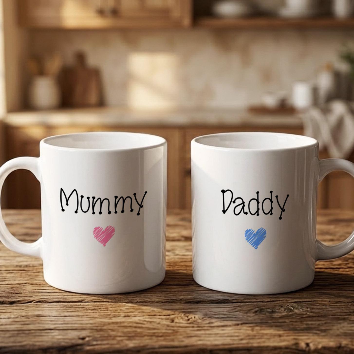 Two white mugs with the names "Mummy" and "Dadmy" printed on them, along with a heart symbol, are placed on a wooden surface.