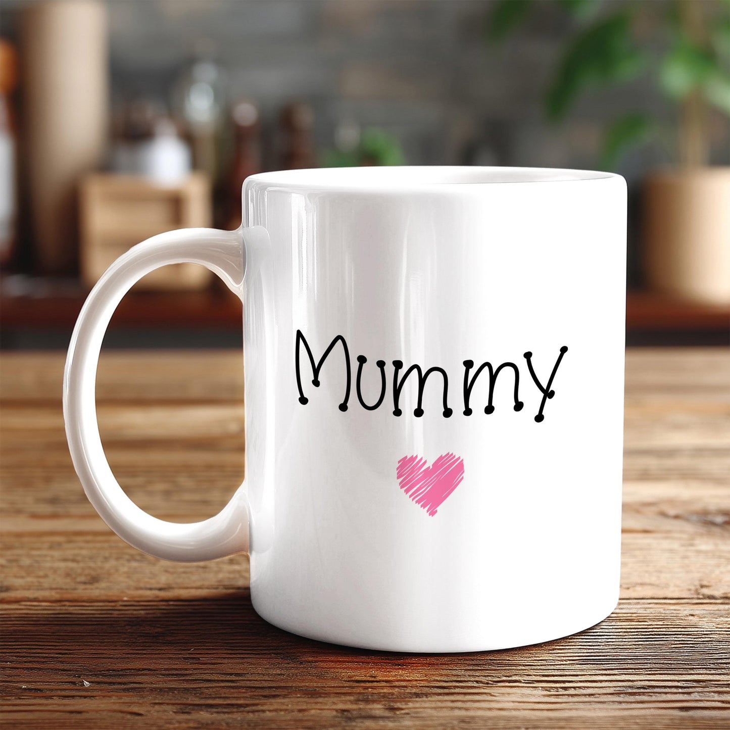 A white ceramic mug with the word "Mummy" written on it, along with a pink heart symbol, sits on a wooden surface.