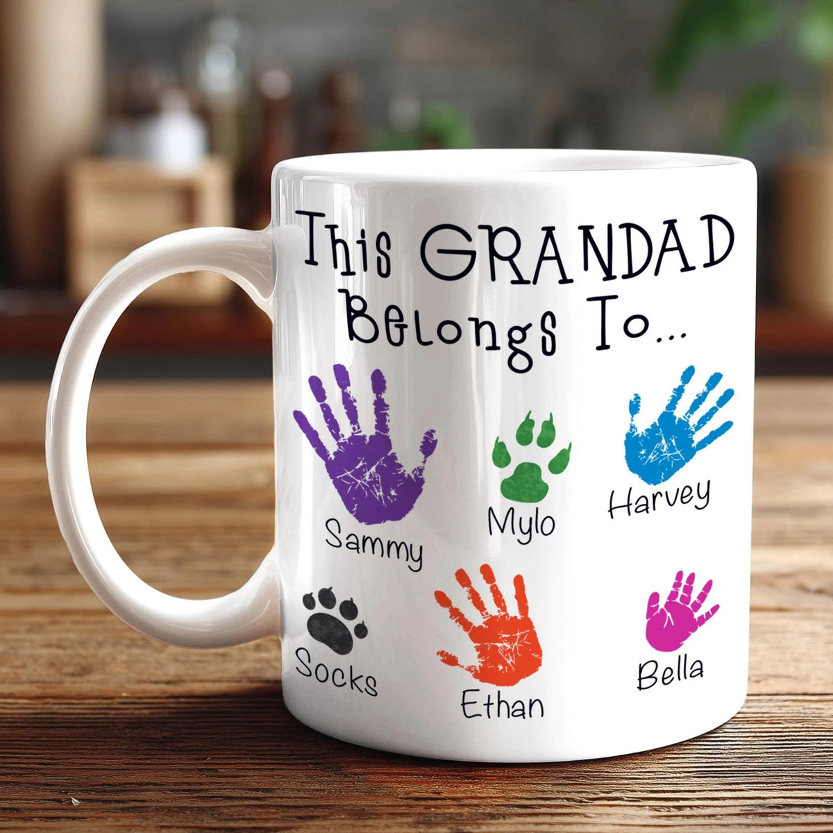 A white mug with a personalized message and handprint designs, placed on a wooden surface.