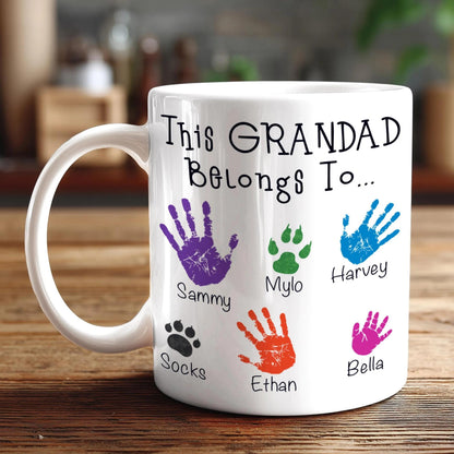 A white mug with a personalized message and handprint designs, placed on a wooden surface.