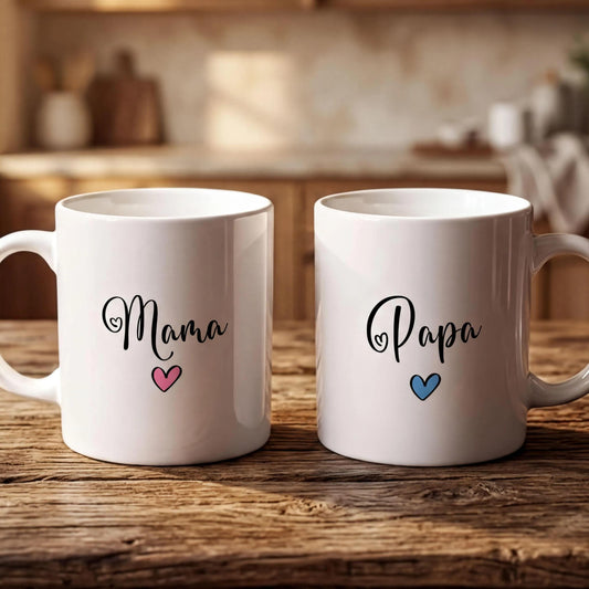 Two white mugs with the names "Mama" and "Papa" printed on them, along with a heart symbol, are placed on a wooden surface.