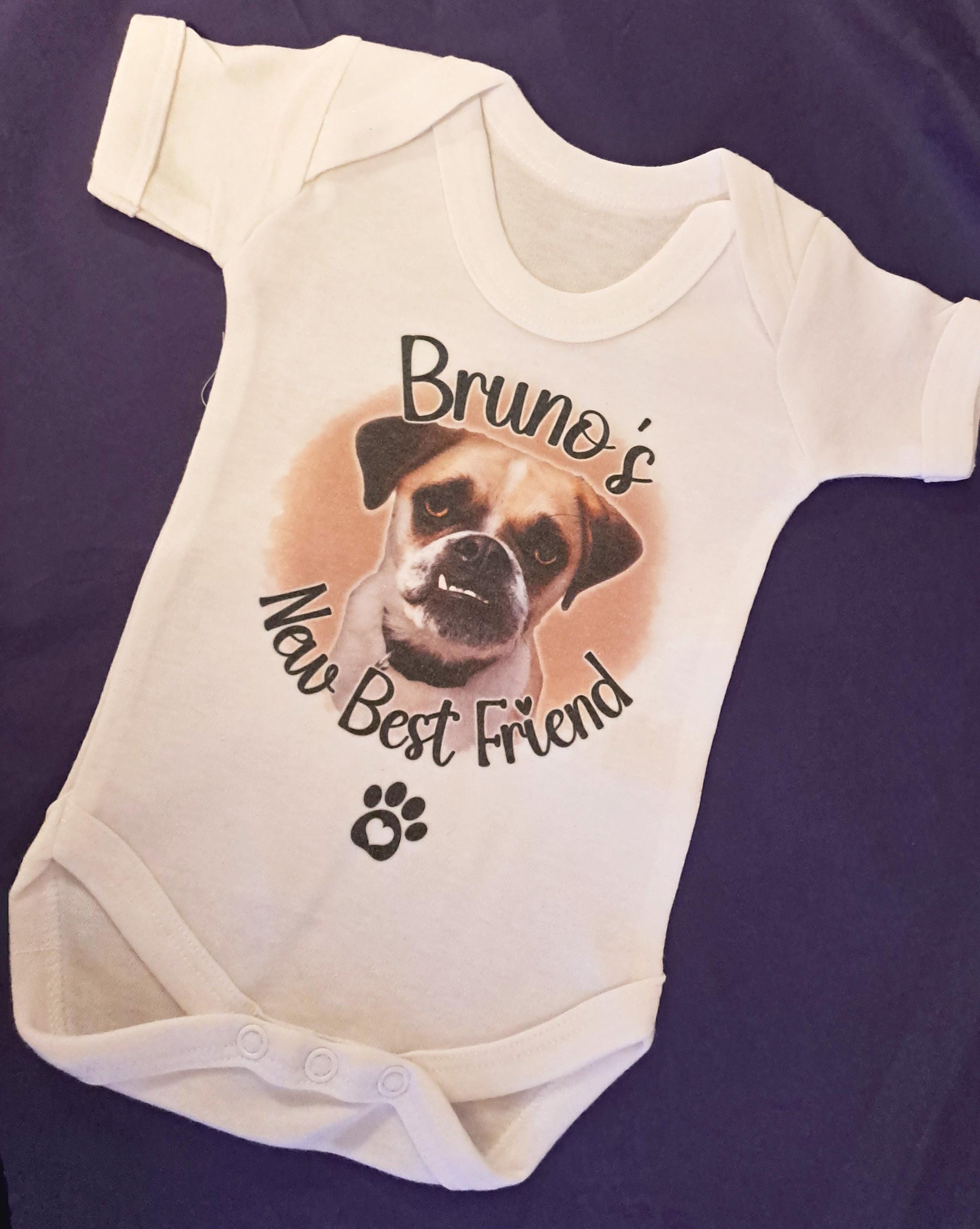 A white baby onesie with a printed image of a dog and the text "Bruno's New Best Friend" printed on it.