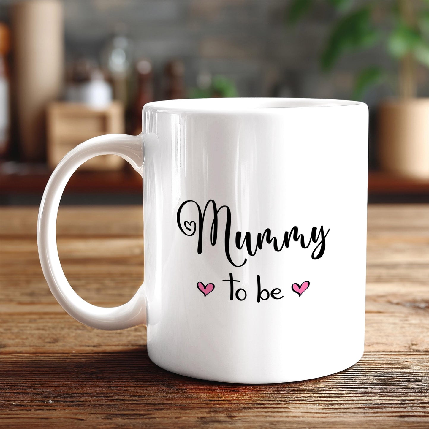 A white ceramic mug with the text "Mummy to be" printed on it, along with two pink heart symbols.