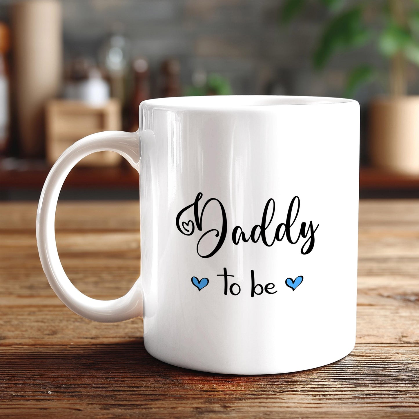 A white ceramic mug with the text "Daddy to be" printed on it, along with two blue heart symbols.