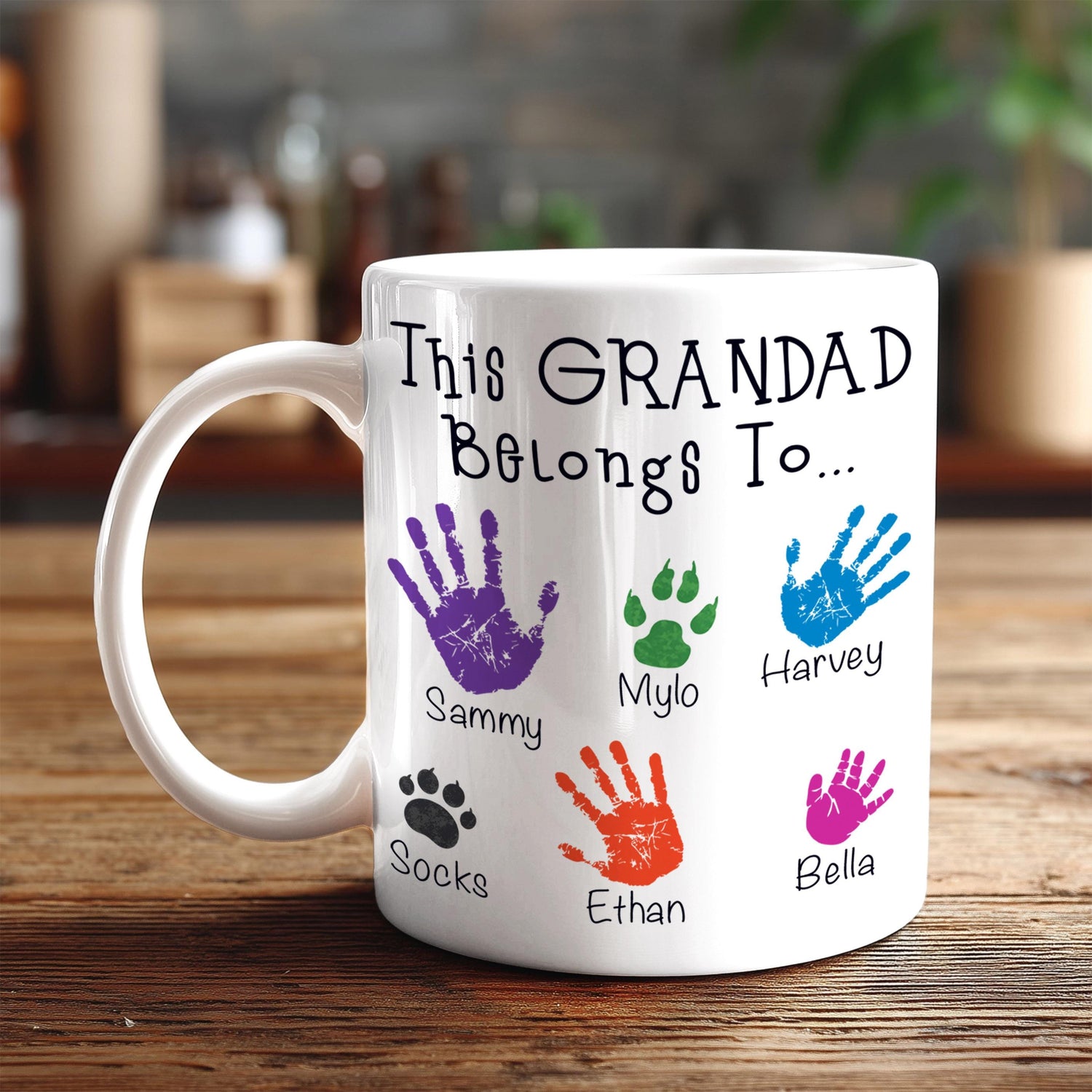 A white mug with a personalized message and handprint designs, placed on a wooden surface.