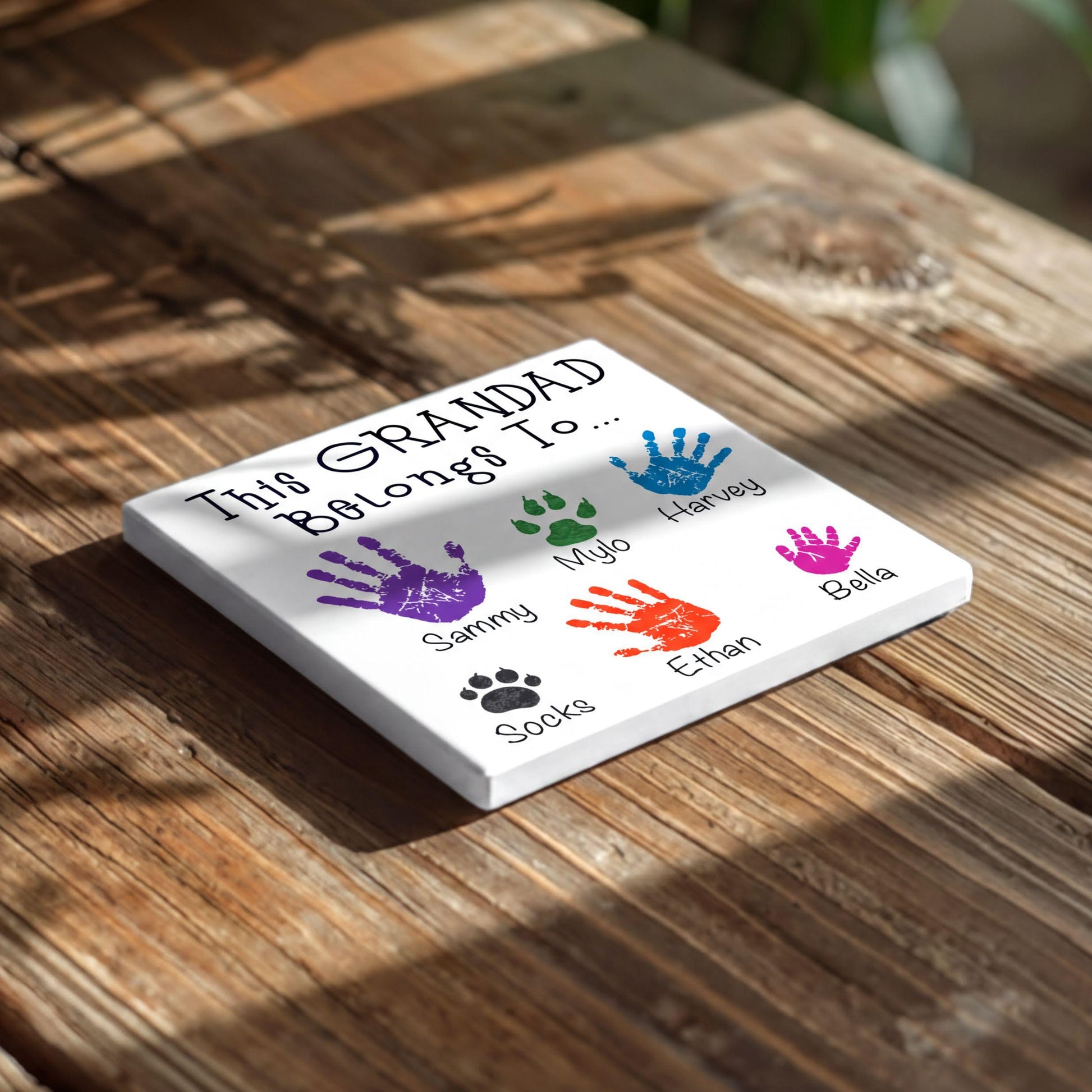 A white sign with handprints and names on it, placed on a wooden surface.