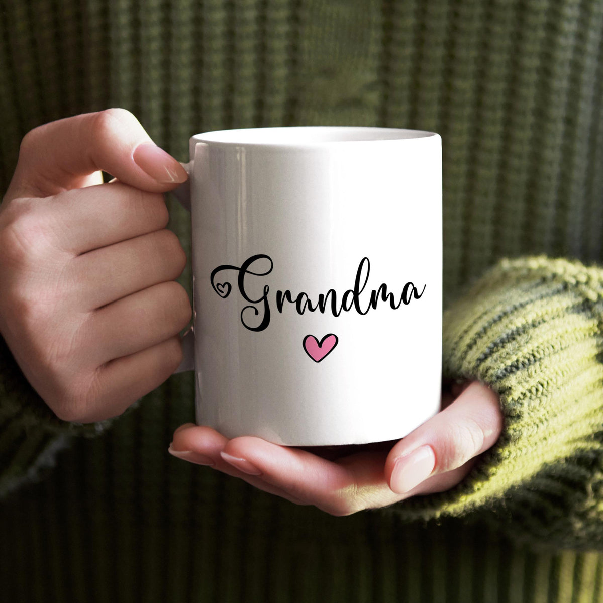A person's hands holding a white mug with the word "Grandma" and a heart symbol printed on it.