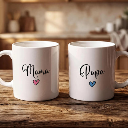 Two white mugs with the names "Mama" and "Papa" printed on them, along with a heart symbol, are placed on a wooden surface.