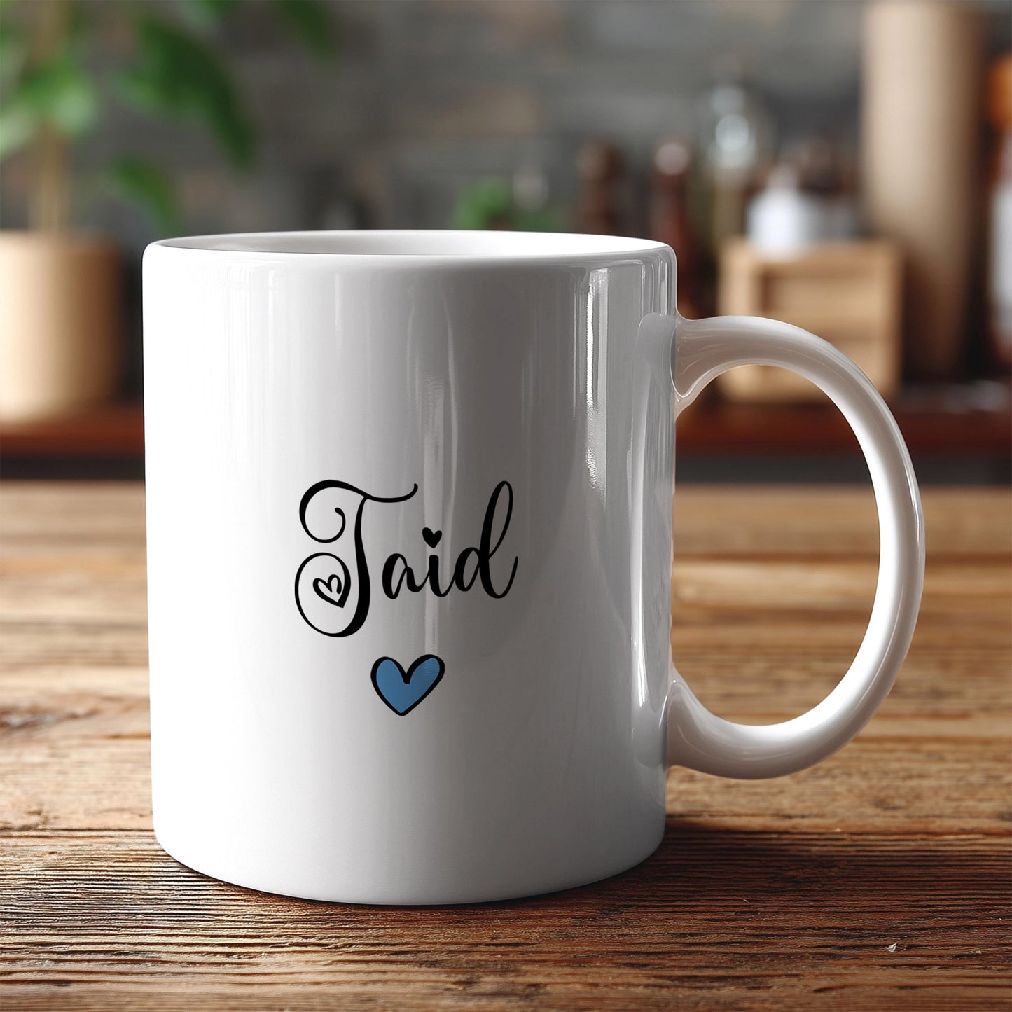 A white ceramic mug with the word "Taid" written on it, along with a small blue heart symbol, sits on a wooden surface.