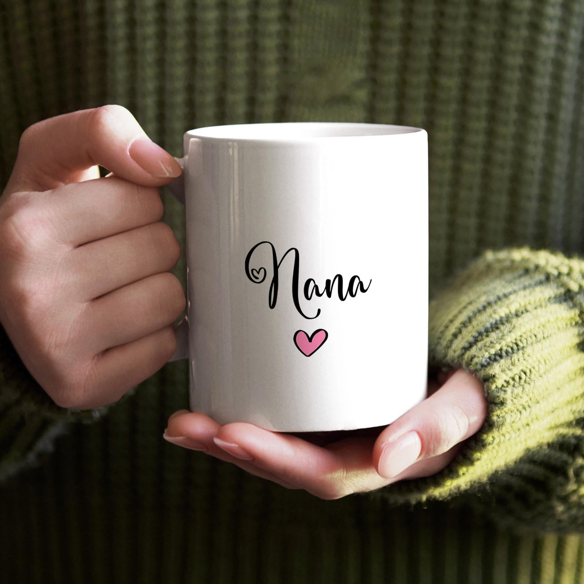 A person's hands holding a white mug with the word "Nana" and a heart symbol printed on it.