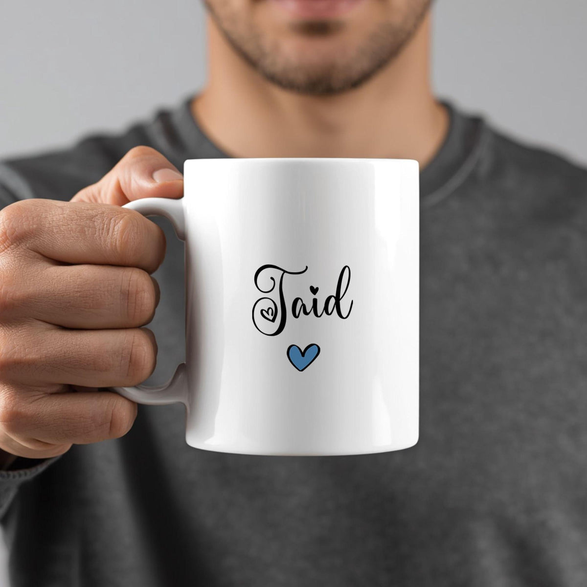 A person is holding a white mug with the word "Taid" written on it, along with a small blue heart symbol.