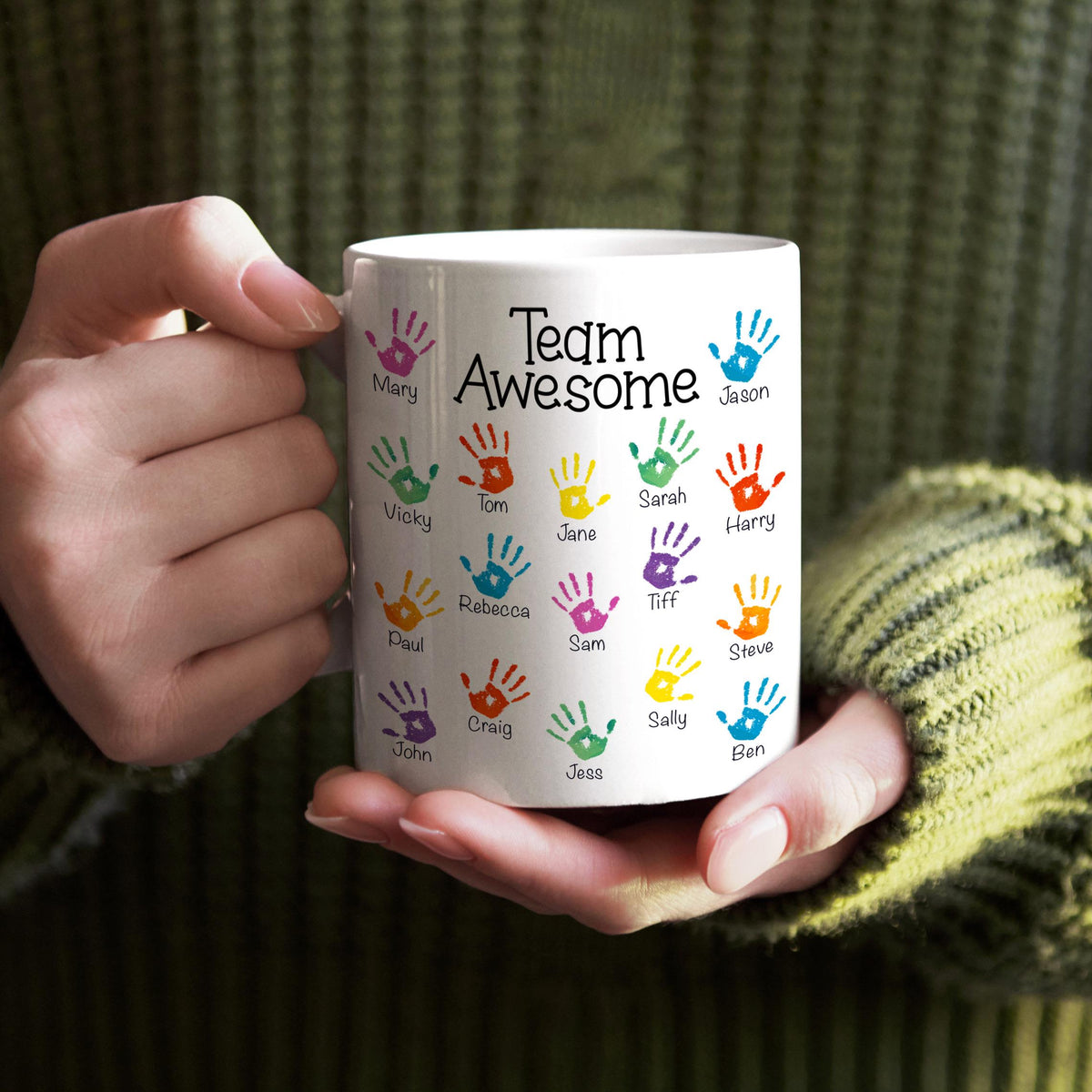A person is holding a white mug with colorful handprints on it, and the mug has the text "Team Awesome" printed on it.