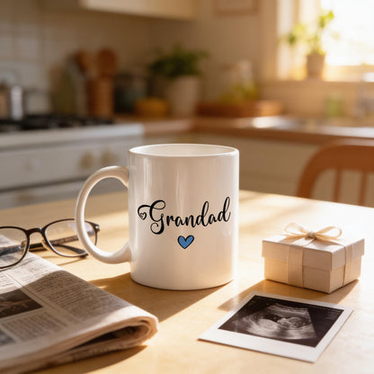 A white mug with the word "Grandad" printed on it, along with a small gift box and a newspaper, sits on a kitchen counter.