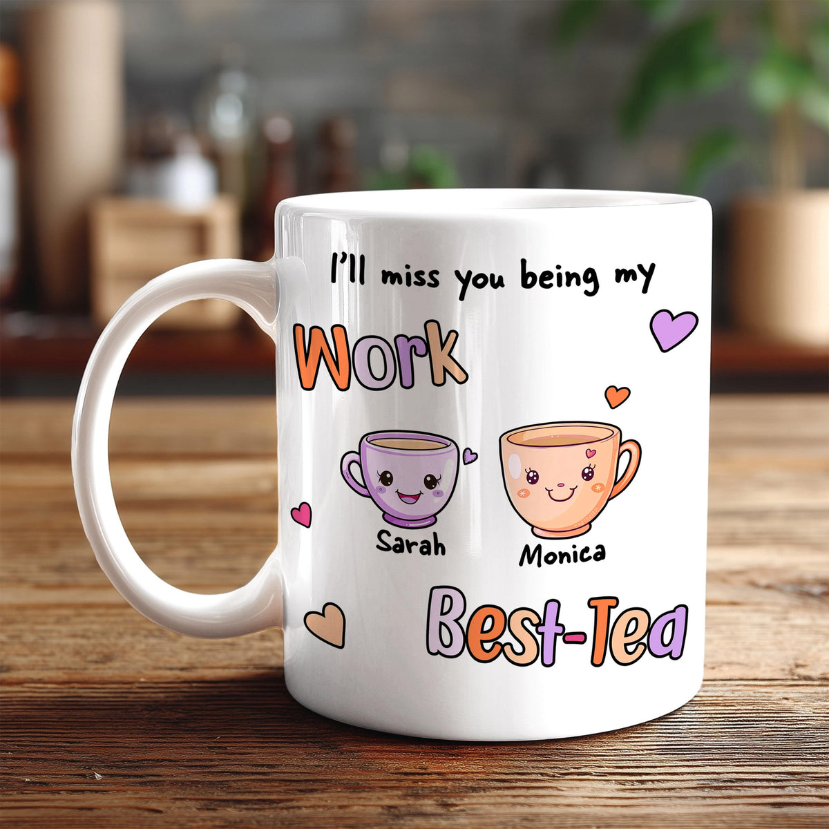 A white coffee mug with a personalized message and illustrations of two cartoon characters, one being Sarah and the other Monica, along with the text "I'll miss you being my Work Best-Tea".