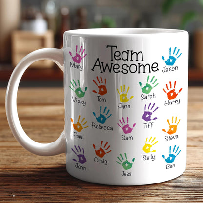 A white coffee mug with colorful handprints and the text "Team Awesome" printed on it.