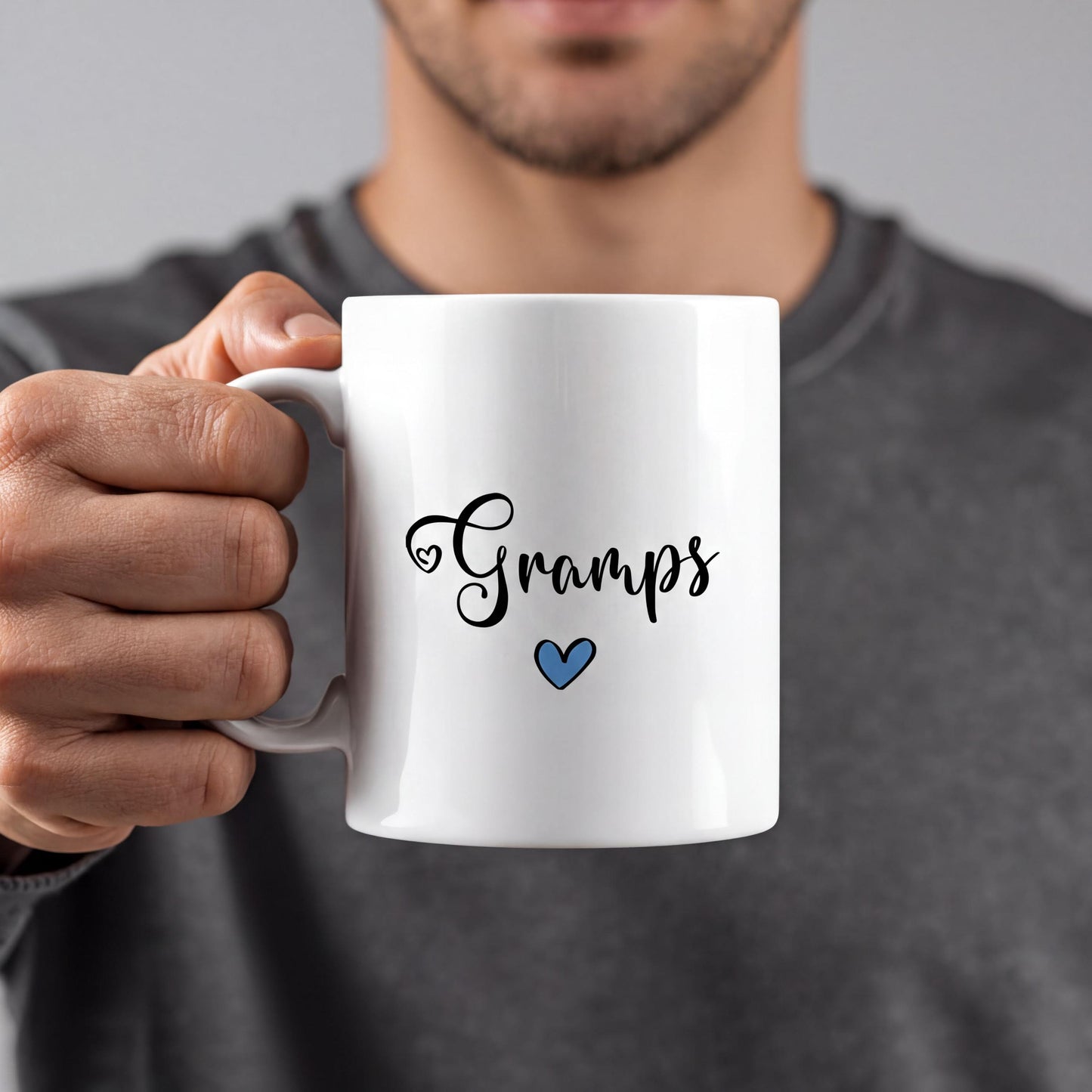 A person is holding a white mug with the word "Gramps" written on it in a cursive font, along with a small blue heart symbol.