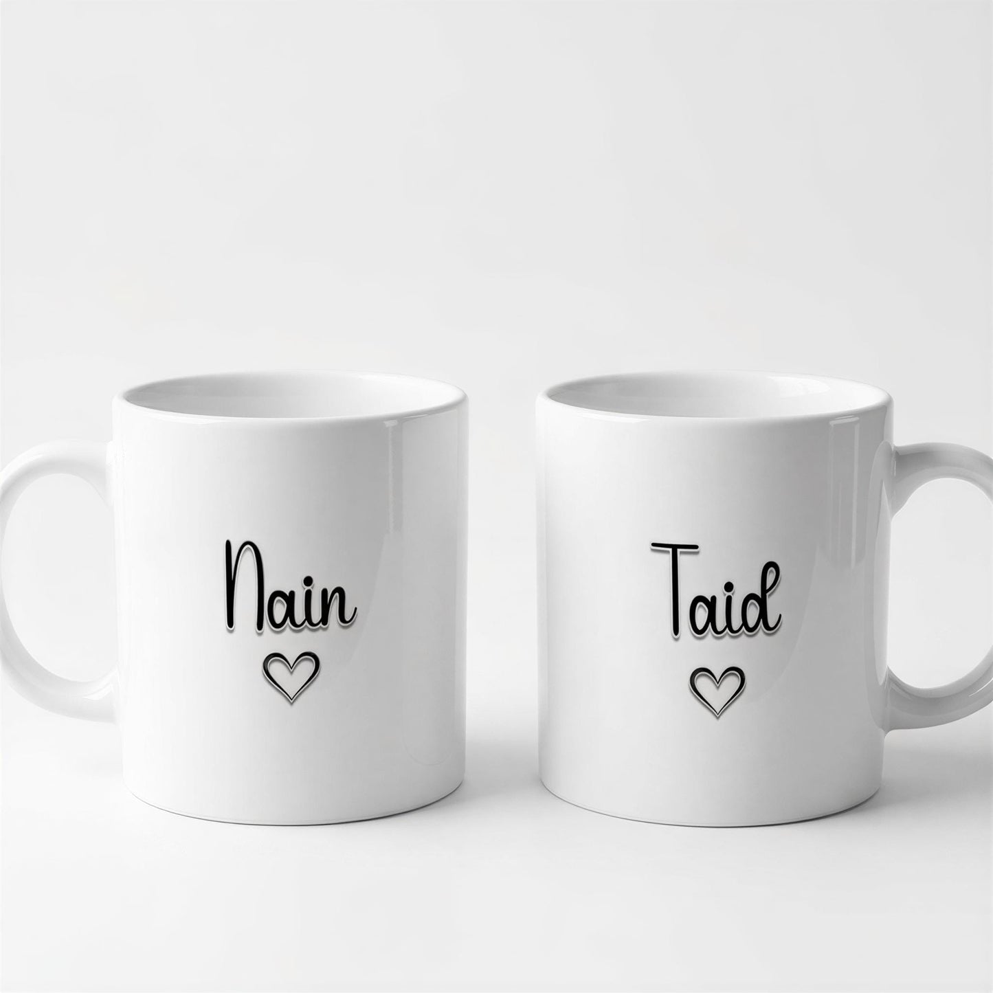 Two white ceramic mugs with black text and heart symbols on them.