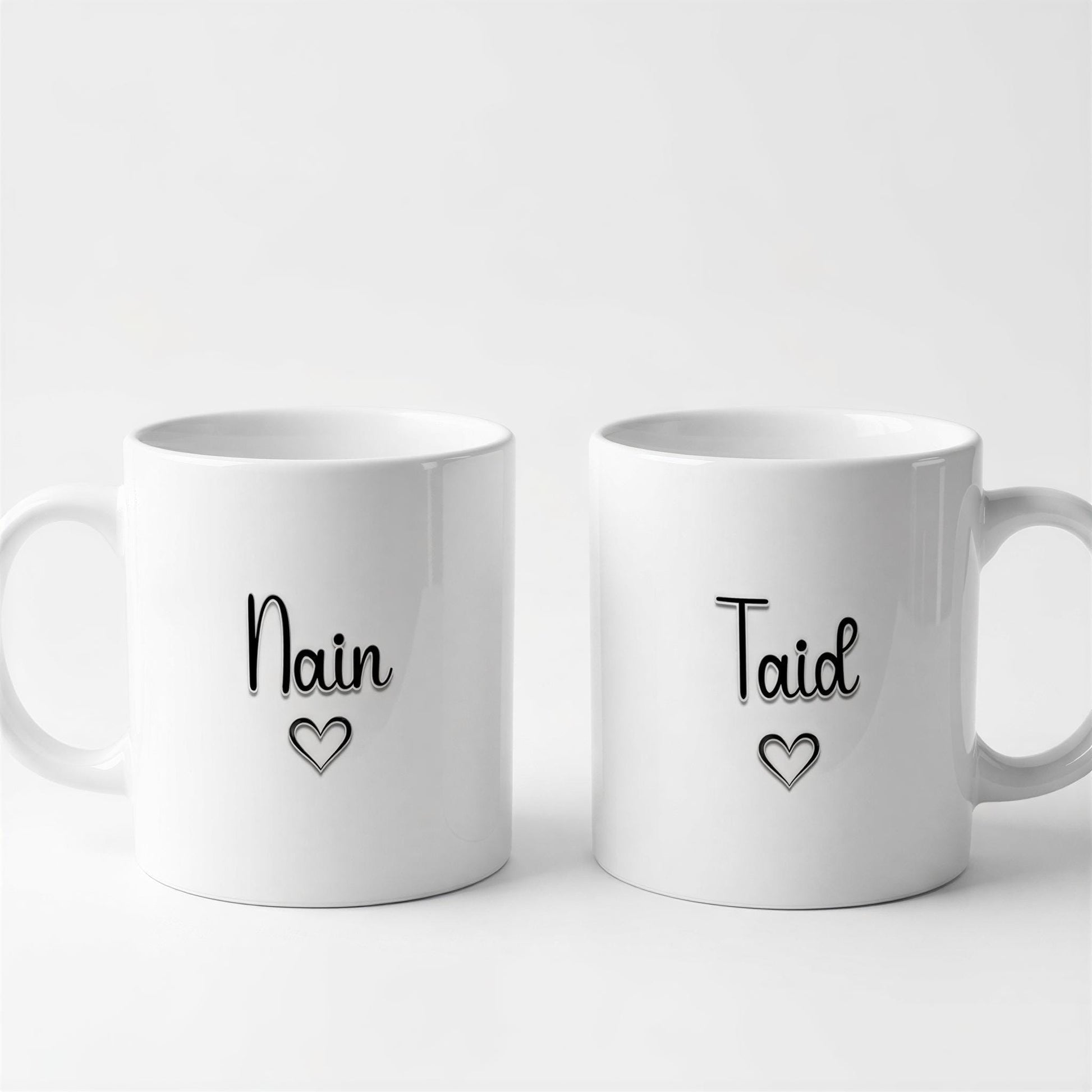Two white ceramic mugs with black text and heart symbols on them.