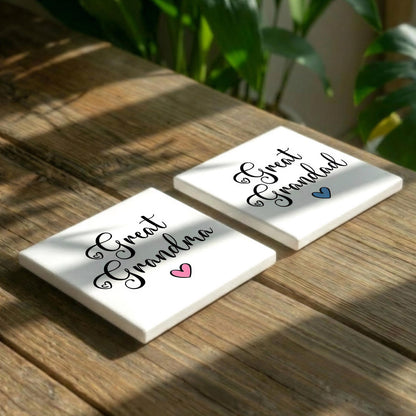 Two white coasters with the text "Great Grandma" printed on them, placed on a wooden surface with some greenery in the background.