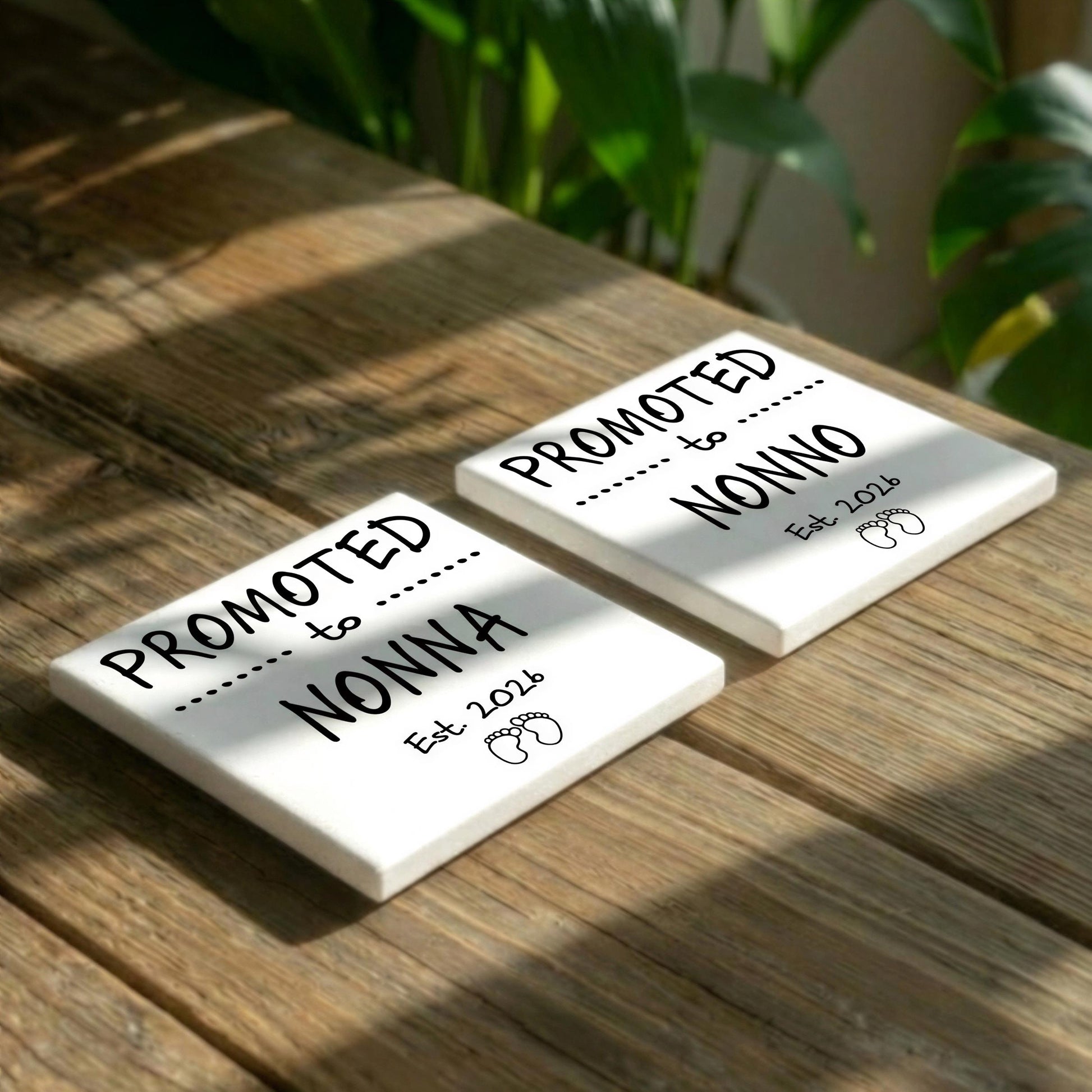 Two white square tiles with black text and graphics placed on a wooden surface, with a plant visible in the background.