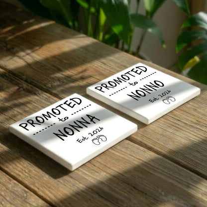 Two white square tiles with black text and graphics placed on a wooden surface, with a plant visible in the background.
