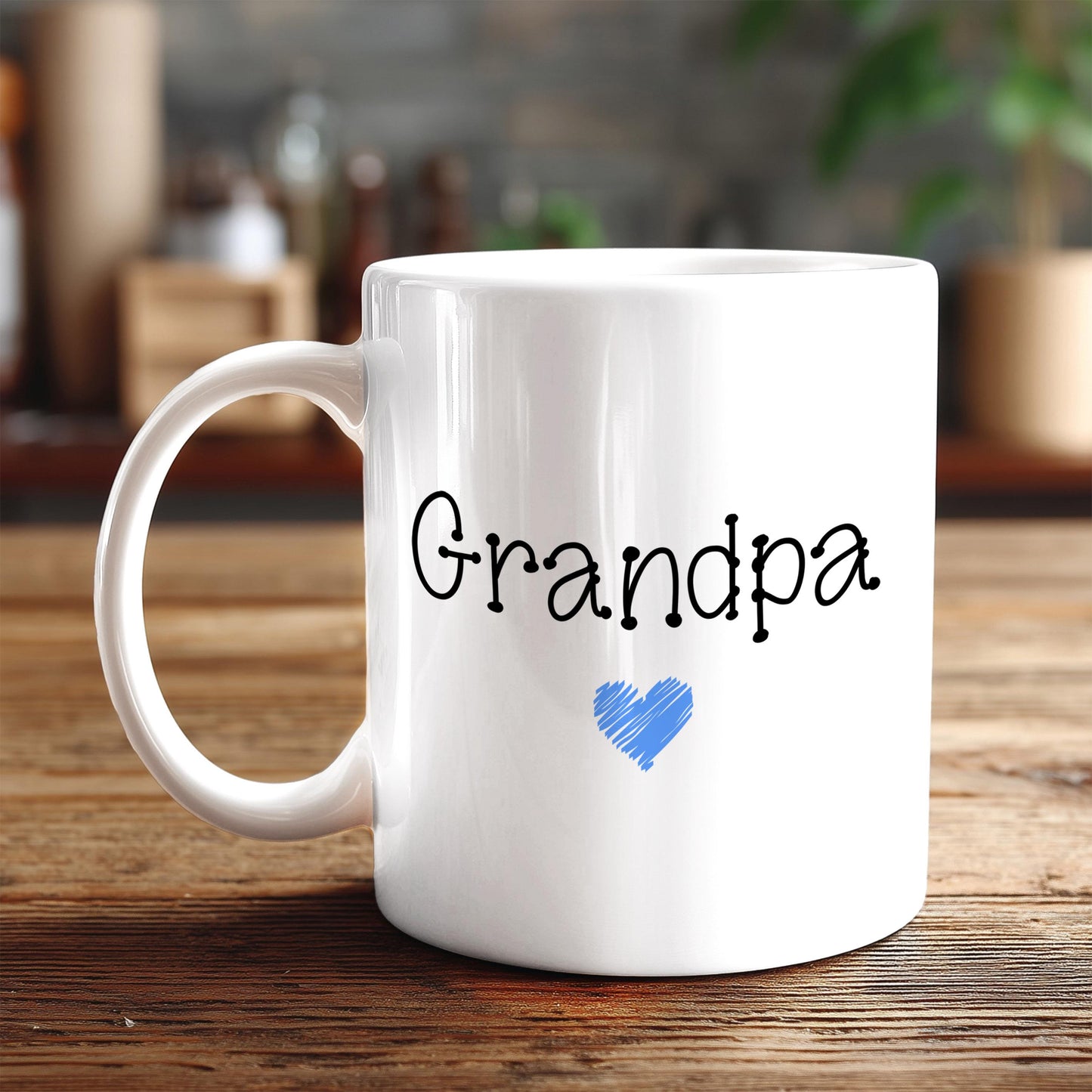 A white ceramic mug with the word "Grandpa" written on it, along with a blue heart symbol, sits on a wooden surface.