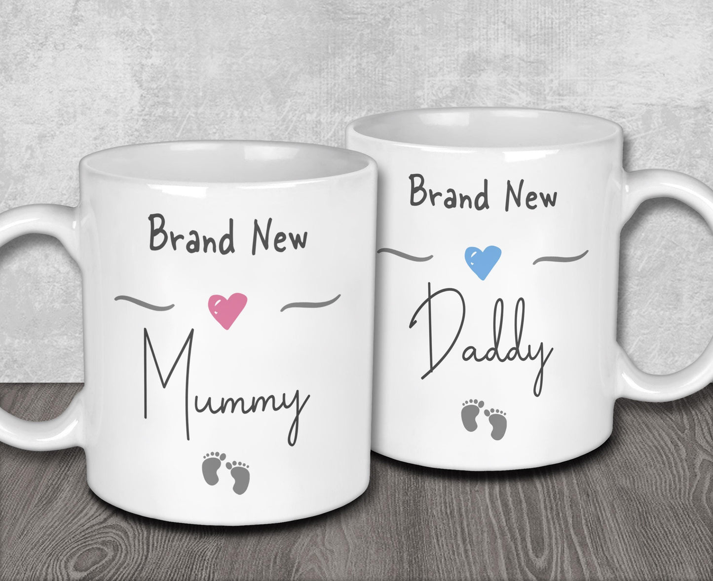Two white ceramic mugs with text and heart symbols on them, one reading "Brand New Mummy" and the other "Brand New Daddy".