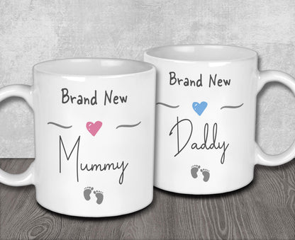Two white ceramic mugs with text and heart symbols on them, one reading "Brand New Mummy" and the other "Brand New Daddy".