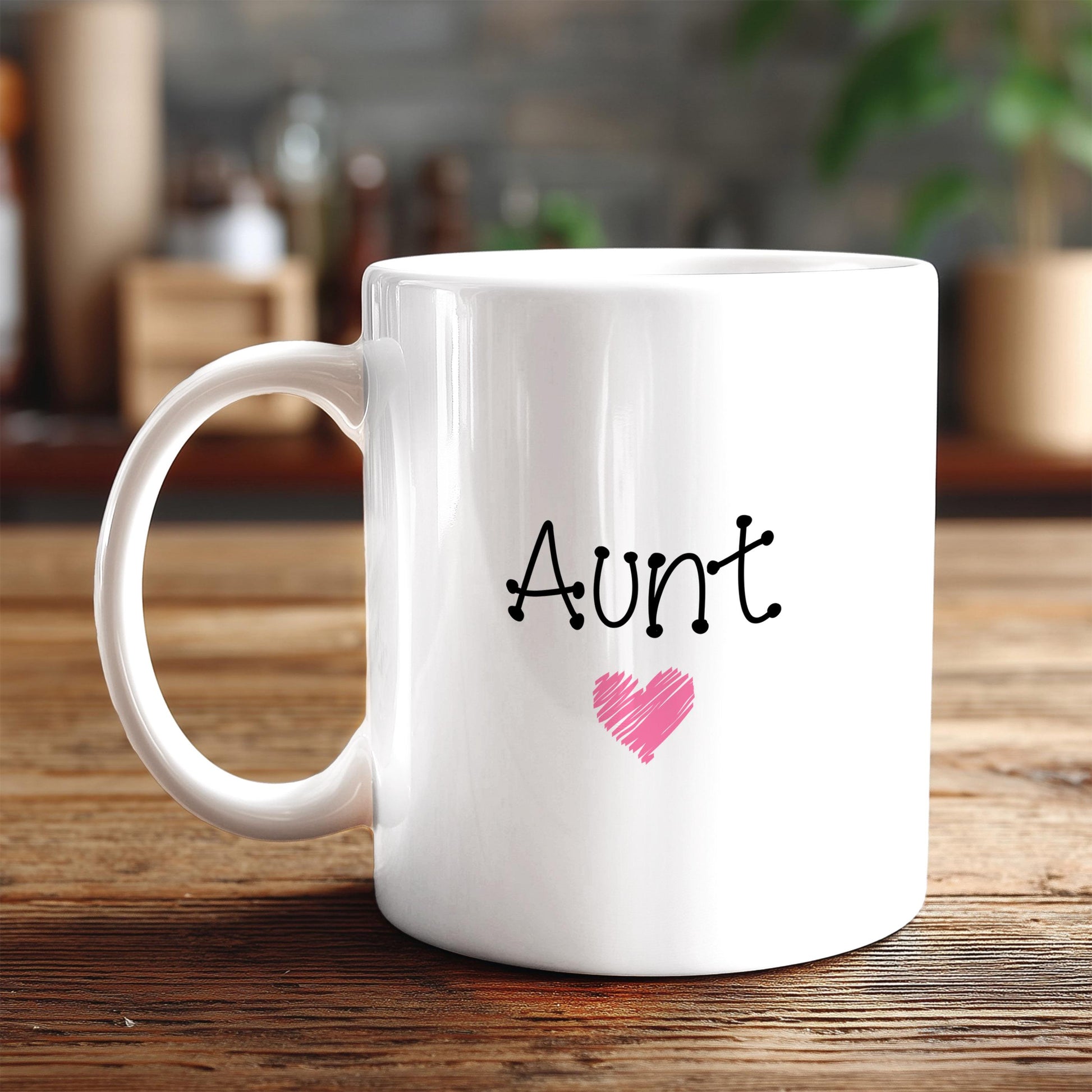 A white ceramic mug with the word "Aunt" and a heart symbol printed on it, placed on a wooden surface.