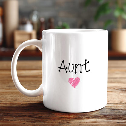 A white ceramic mug with the word "Aunt" and a heart symbol printed on it, placed on a wooden surface.