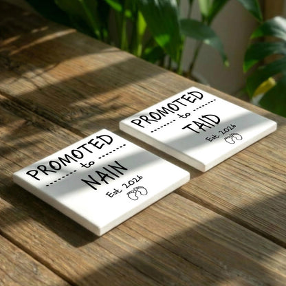 Two white square tiles with black text and graphics placed on a wooden surface, with a plant in the background.