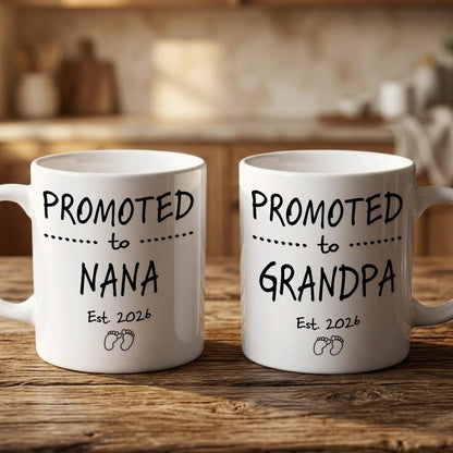 Two white ceramic mugs with black text that reads "PROMOTED TO NANA Est. 2026" and "PROMOTED TO GRANDPA Est. 2026" printed on them.