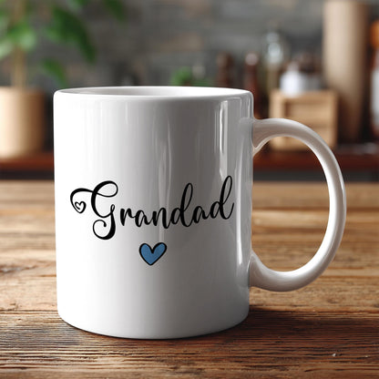 A white ceramic mug with the text "Grandad" and a blue heart printed on it, placed on a wooden surface.