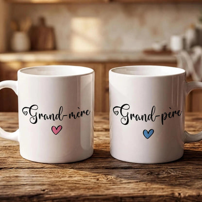 Two white mugs with the text "Grand-more" and "Grand-pire" printed on them, placed on a wooden surface.