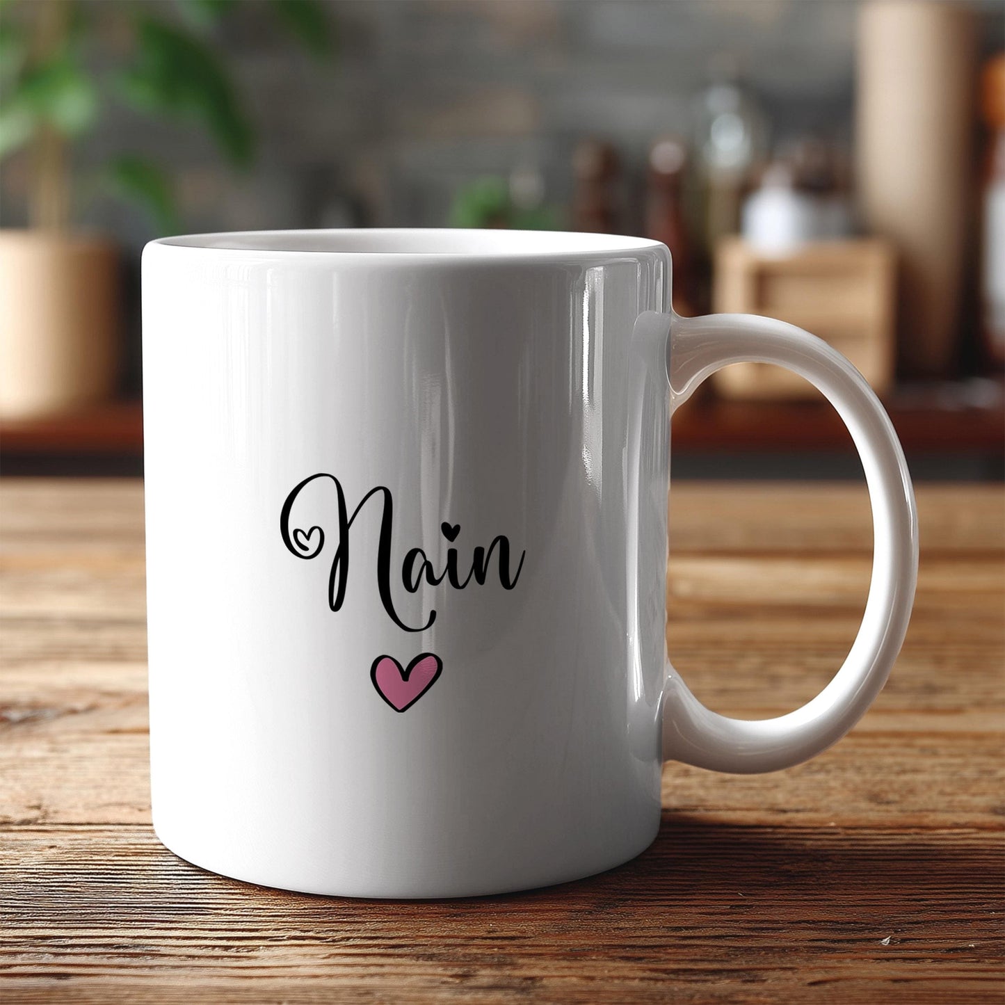 A white ceramic mug with the name "Nain" and a heart symbol printed on it, placed on a wooden surface.