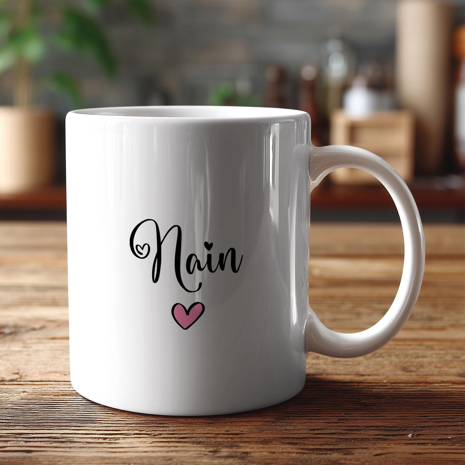 A white ceramic mug with the name "Nain" and a heart symbol printed on it, placed on a wooden surface.