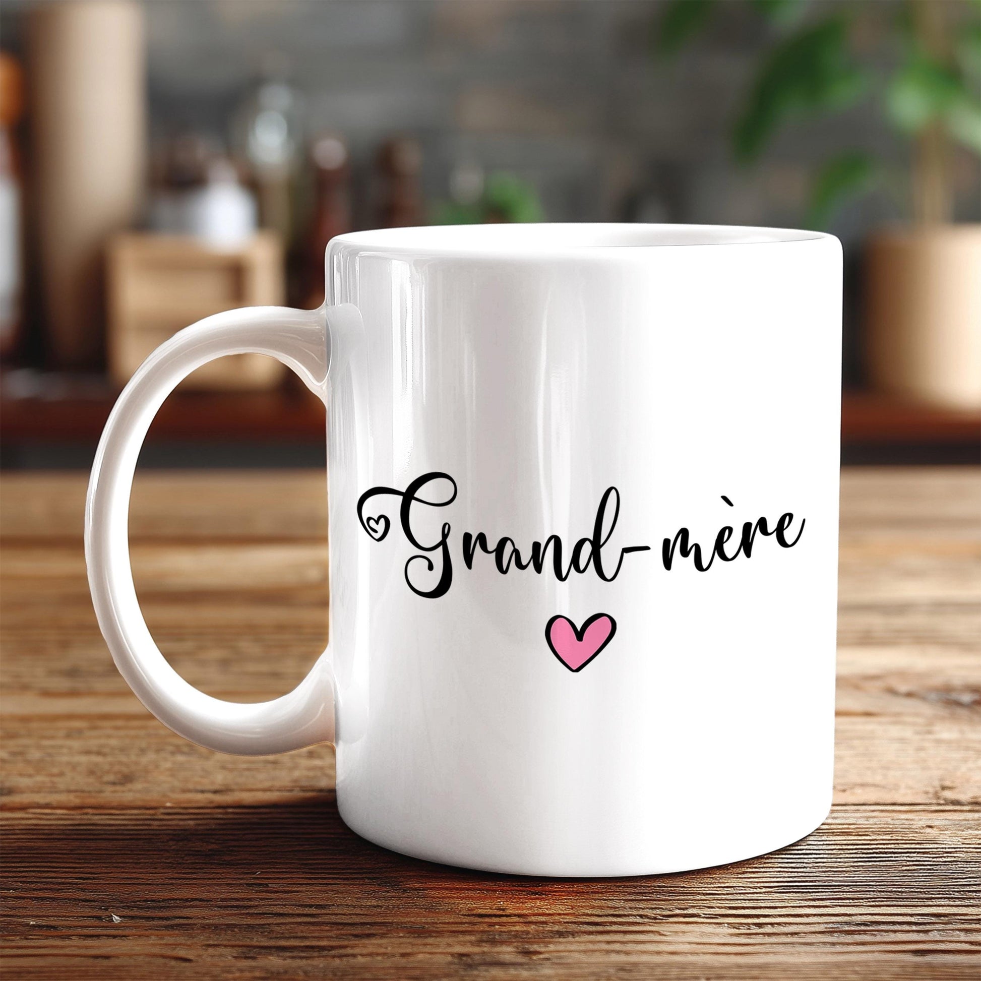 A white ceramic mug with the text "Grand-mère" and a heart symbol printed on it, placed on a wooden surface.