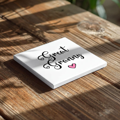 A white square coaster with the text "Great Grandma" and a pink heart on it, placed on a wooden surface.